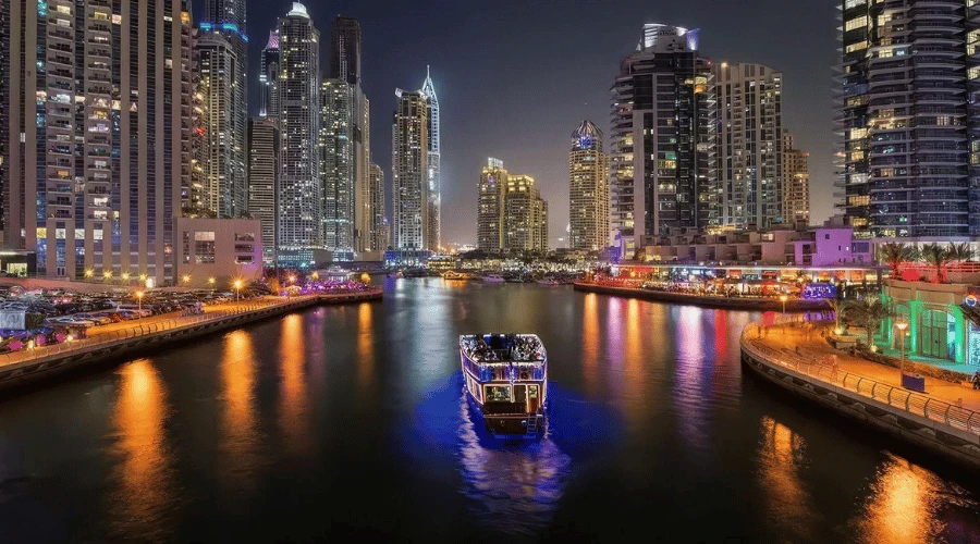 Illuminated luxury dhow cruise sailing across the Dubai Marina canal at night surrounded by glowing skyscrapers.