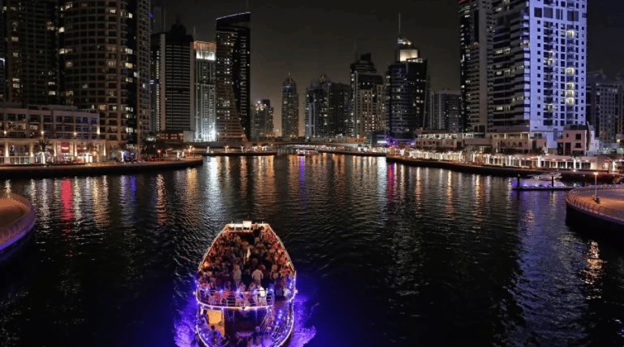 Top-angle view of a lit dinner dhow cruise cruising through the tranquil waters of Dubai Marina canal.