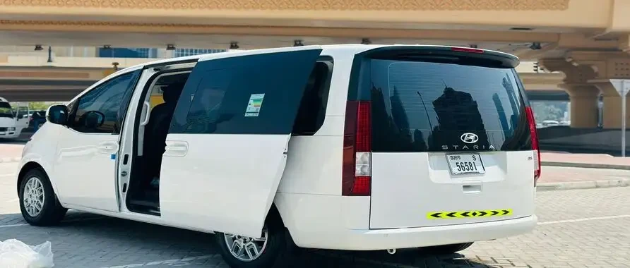 A white Hyundai Staria Comfort van with its door open, positioned outside a building, ready for rentals in Dubai.