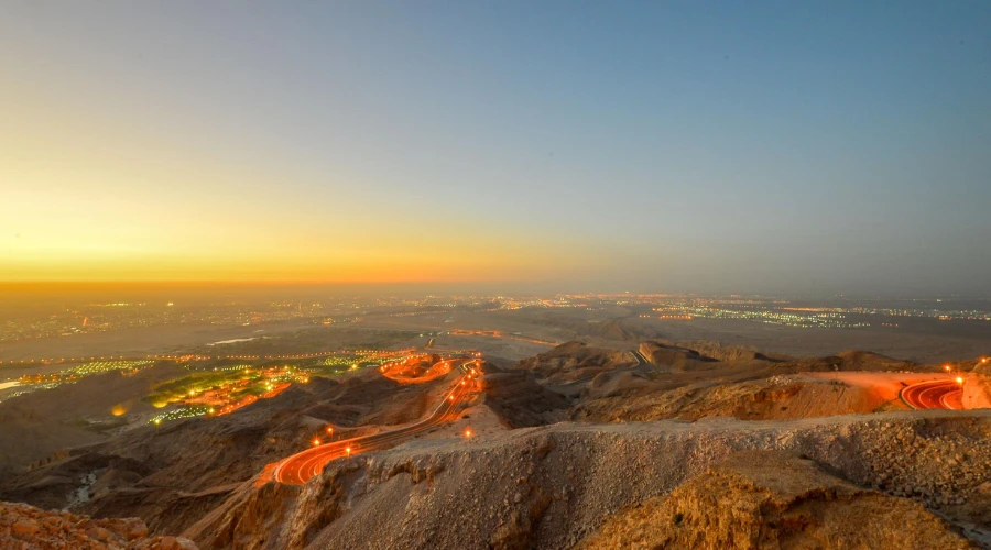 Panoramic sunset view of illuminated winding mountain road from Jebel Hafeet peak overlooking Al Ain