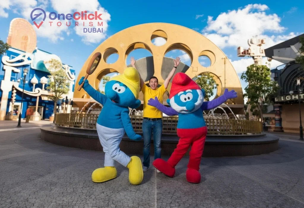 A happy man with arms raised posing between two colorful Smurf characters at a Motiongate Dubai park attraction.