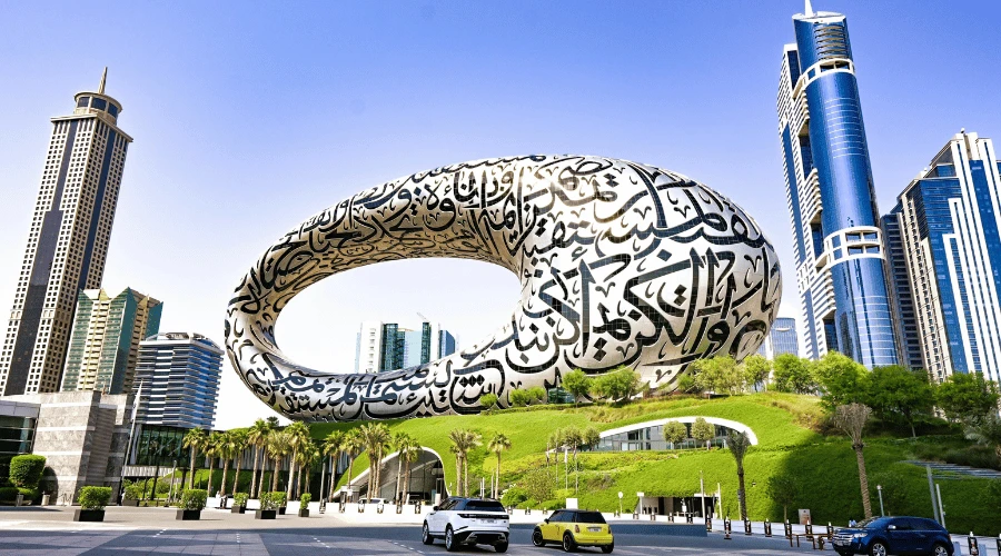 Iconic torus-shaped exterior of the Museum of the Future adorned with intricate Arabic calligraphy against a blue sky.