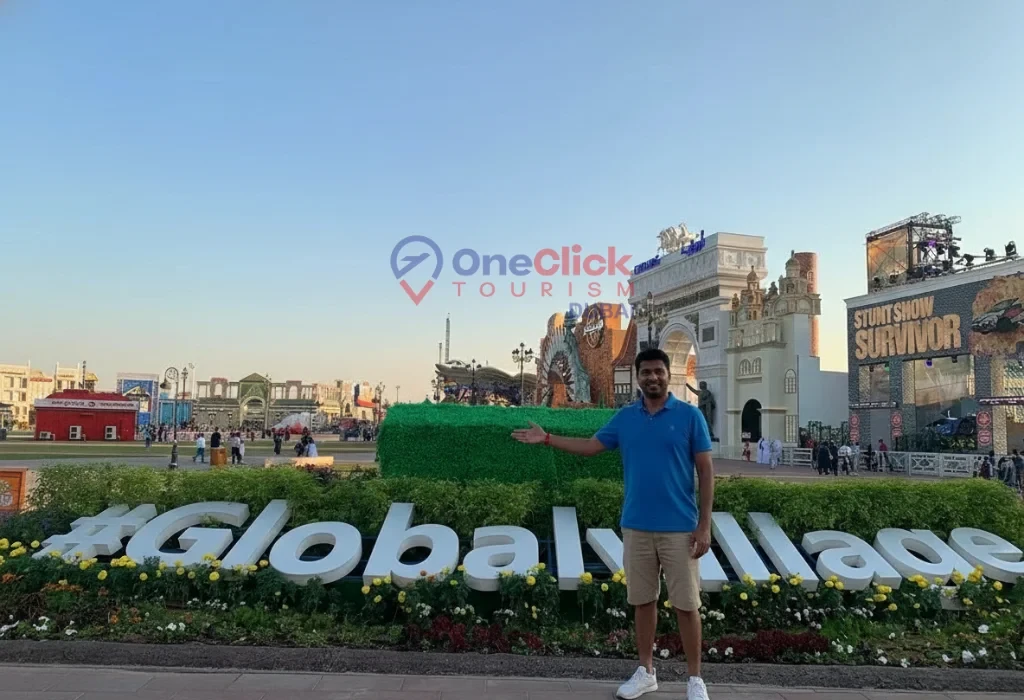 A man pointing toward the Global Village sign with the OneClick Tourism Dubai logo overlay.