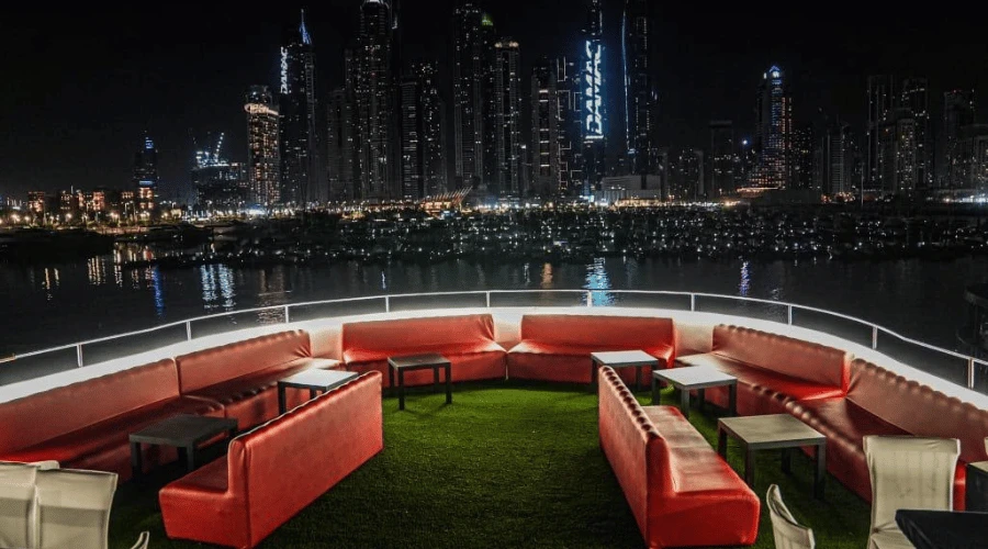 Open-air upper deck lounge with red leather sofas and skyline views on a Dubai Marina dhow cruise.