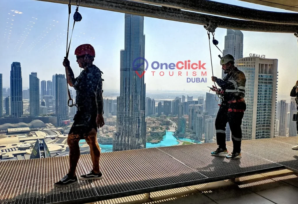 Tourists wearing safety harnesses and helmets preparing for the Sky Walk Dubai experience on an external ledge overlooking the Burj Khalifa.