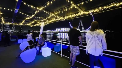 Sightseers relaxing on the cruise lounge deck with panoramic nighttime views of Ain Dubai on Bluewaters Island.