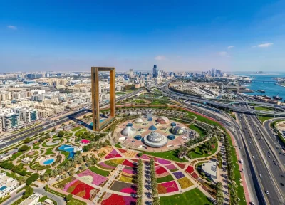 A wide-angle landscape shot of the golden Dubai Frame standing tall over Zabeel Park, with the city skyline and highway infrastructure in the background.