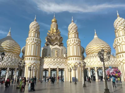 The ornate, white and gold domed entrance of Global Village in Dubai with crowds of people walking through.