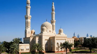 White stone facade, central dome, and tall twin minarets of the historic Jumeirah Mosque under a clear blue sky.