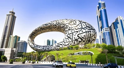 Iconic torus-shaped exterior of the Museum of the Future adorned with intricate Arabic calligraphy against a blue sky.