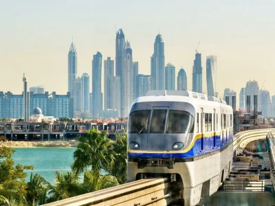 The Palm Jumeirah Monorail train traveling on an elevated track with the modern high-rise skyscrapers of the Dubai Marina skyline in the background.